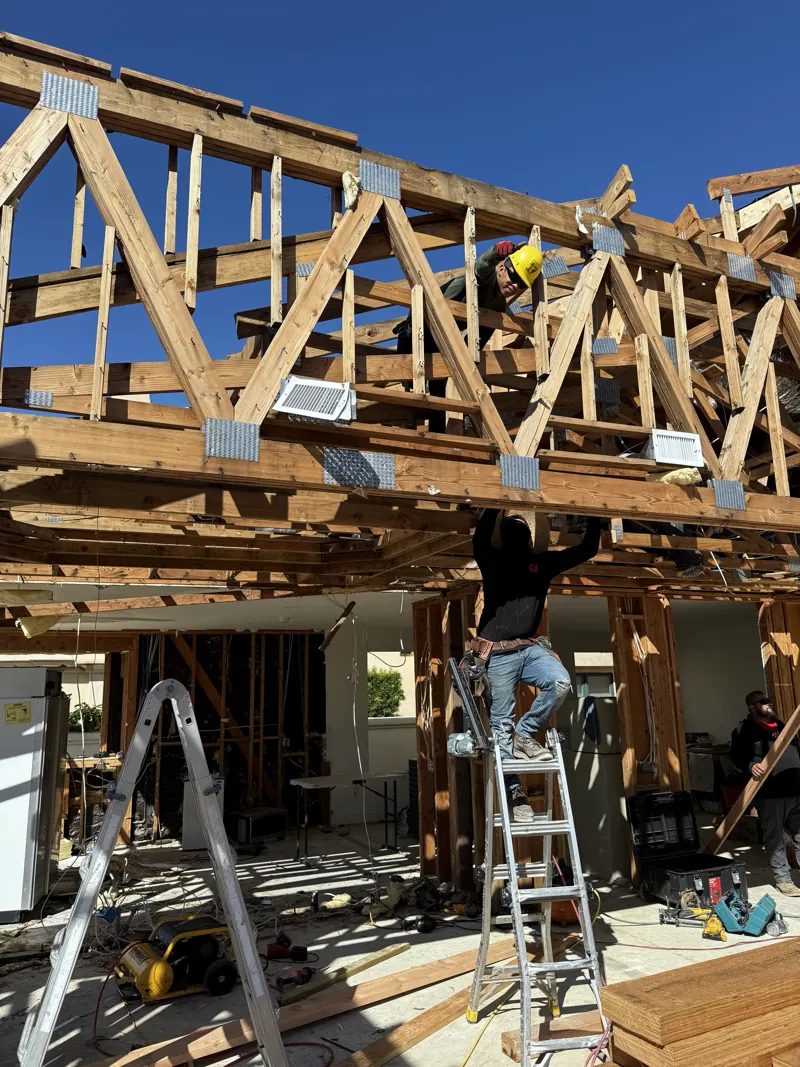 Crew installing roof trusses from ladders inside the open frame